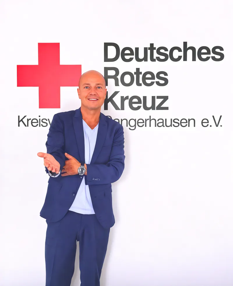 Herr Claus :D Ein Mann im Anzug der Sympathisch Lächelt und Vor dem DRK Logo platziert ist